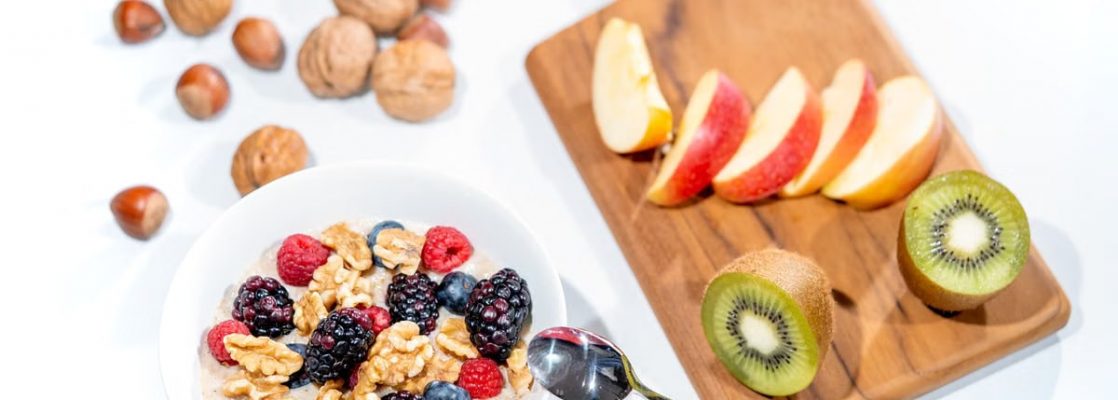 A nutritious breakfast bowl featuring fresh berries and walnuts, served with sliced fruit and kiwi.
