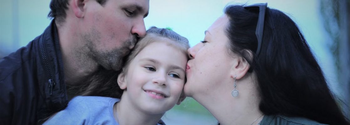 A heartwarming capture of parents showing love to their smiling daughter with gentle kisses.