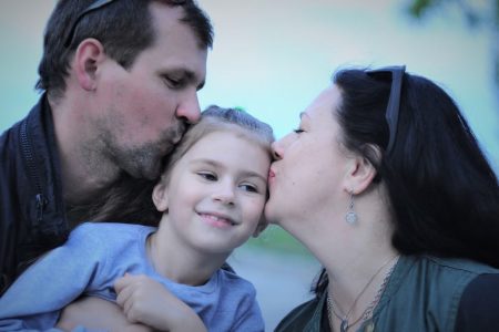 A heartwarming capture of parents showing love to their smiling daughter with gentle kisses.