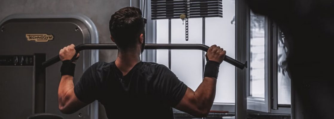 Back view of a man exercising with lat pulldown machine in the gym.