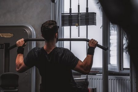 Back view of a man exercising with lat pulldown machine in the gym.