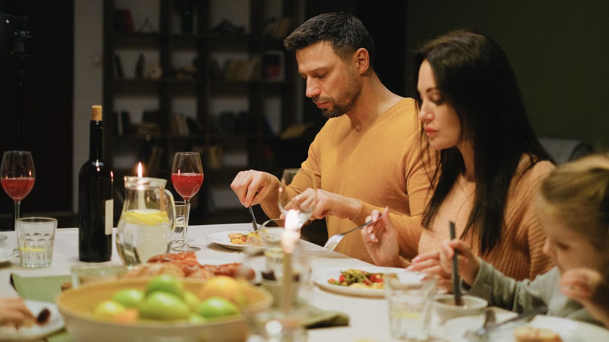 A family gathered around a dinner table indoors, enjoying a meal together with wine and candles.